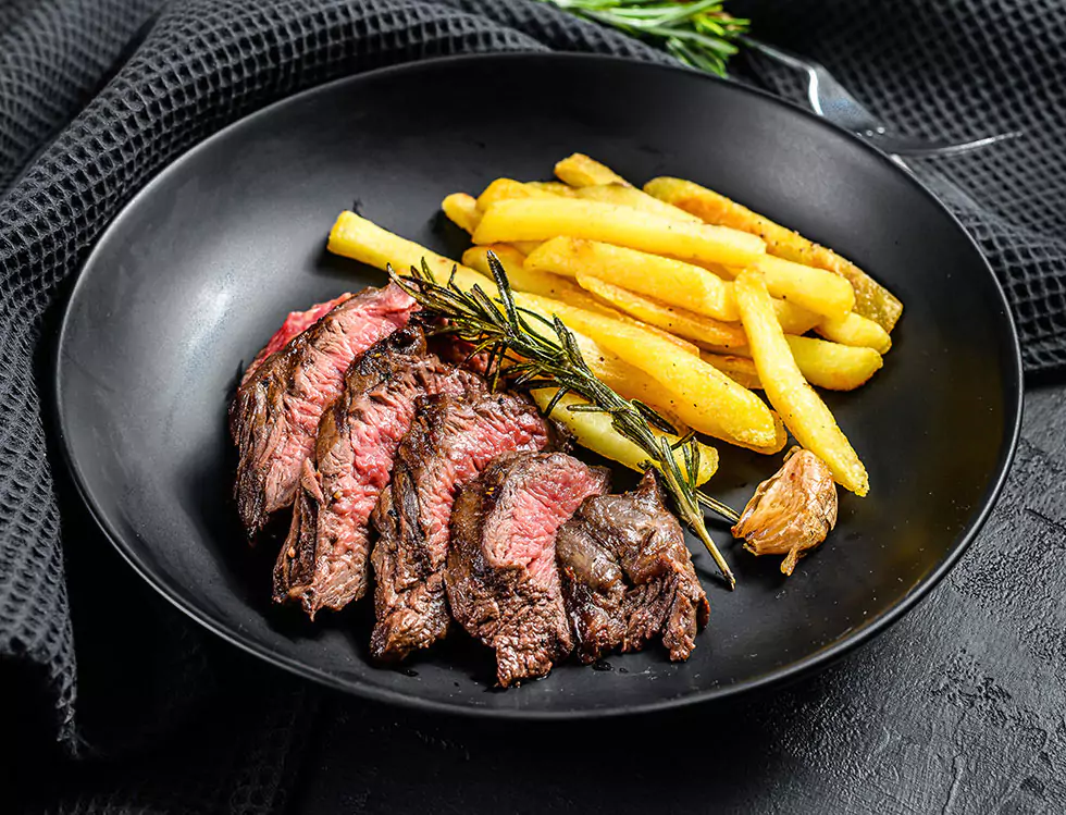 Aufgeschnittenes Steak mit Pommes frites auf Schwarzem Hintergrund